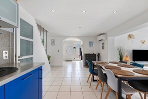 A modern kitchen with blue cabinets, a dining area with a table and chairs, and a TV on the wall.