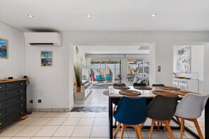 A dining area with a table set for four, surrounded by chairs, and a kitchen area with a white cabinet and a painting on the wall.