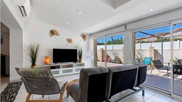 A modern living room with a flat-screen TV, comfortable seating, and a large sliding glass door leading to an outdoor patio.