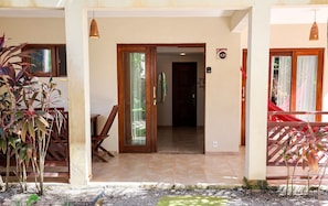 Entrada de um hotel com porta de madeira, soalho em azulejos e um pequeno jardim com plantas.