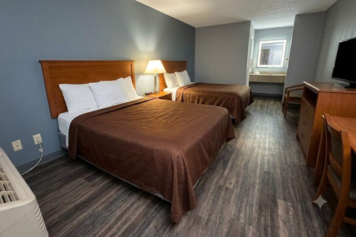 Camera d'albergo con due letti, una scrivania, una TV e una finestra.