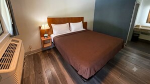 Una habitación de hotel con cama, mesita de noche, lámpara y ventana con cortinas.