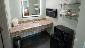 Un baño con encimera de granito, un lavamanos, un espejo con luz, toallero, calefactor y microondas.