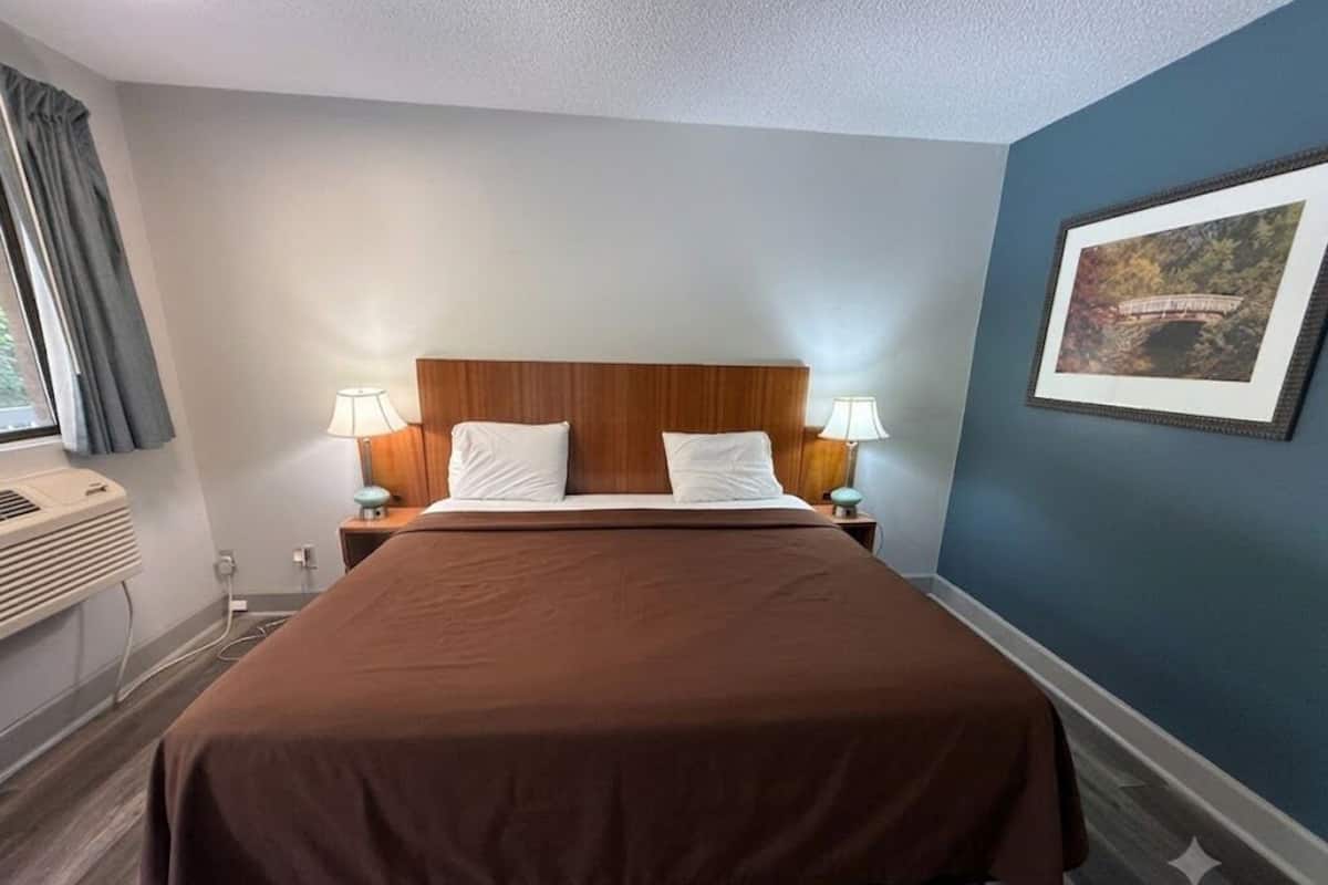 Una camera d'albergo con un letto grande, due abat-jour, un quadro incorniciato appeso al muro e una finestra con tende.