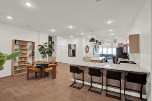 A modern kitchen with a central island, bar stools, and a dining area with a round table and chairs. - 1BR Downtown Suite | Pool, Gym & Workspace (Cincinnati)