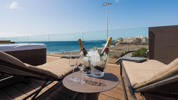 Eine Dachterrasse mit Blick auf den Strand, zwei Champagnerflaschen und zwei Gläser auf einem Tisch.