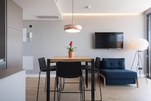 A modern living room with a TV, a dining table with chairs, a sofa, a potted plant, and a pendant light.