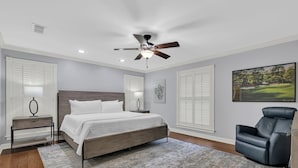 Une chambre à coucher avec un lit, un ventilateur de plafond, une table de chevet, une chaise et un tableau accroché au mur.