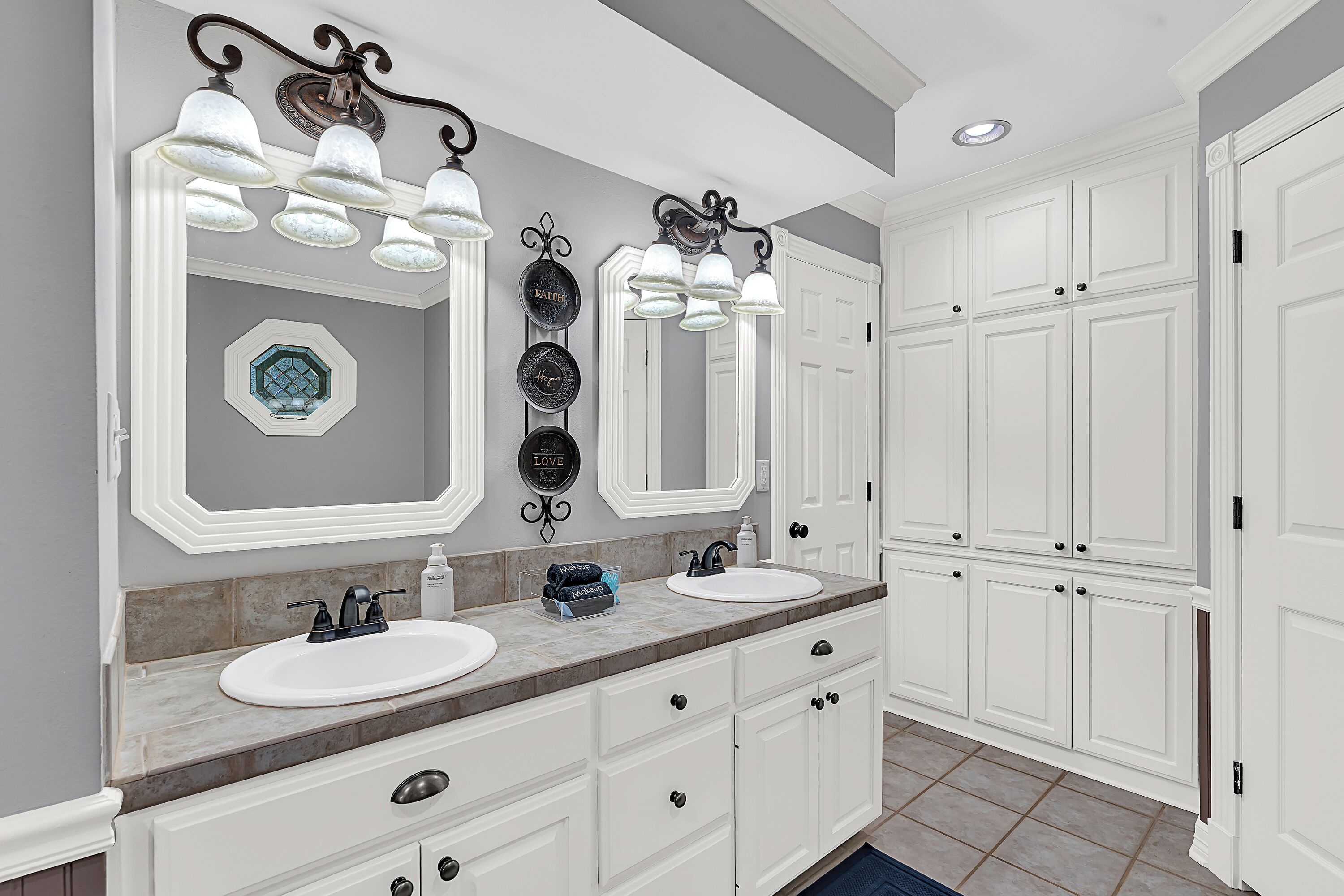 Une salle de bain avec deux lavabos, un meuble-lavabo avec des tiroirs, un grand miroir et un luminaire au plafond.