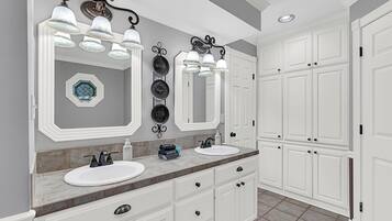 Une salle de bain avec deux lavabos, un meuble-lavabo avec des tiroirs, un grand miroir et un luminaire au plafond.