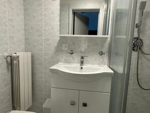 Un baño con lavamanos, espejo y ducha blancos.