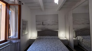 Un dormitorio con una cama, dos mesitas de noche, una ventana con cortinas y un cuadro de un puente.