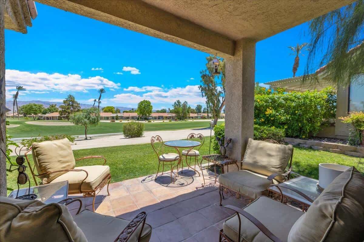 A covered patio with outdoor furniture, a table, and a view of a golf course.