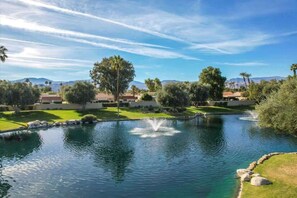 A serene outdoor pool area with a fountain, surrounded by well-maintained lawns and trees. - Palm Breeze | 3BR Resorter (Palm Desert)