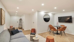 A modern living room with a sofa, a dining table with chairs, a TV, and a mirror on the wall. - COMBINING COMFORT, TRANQUILITY & A PRIME LOCATION MONTMARTRE (Paris)