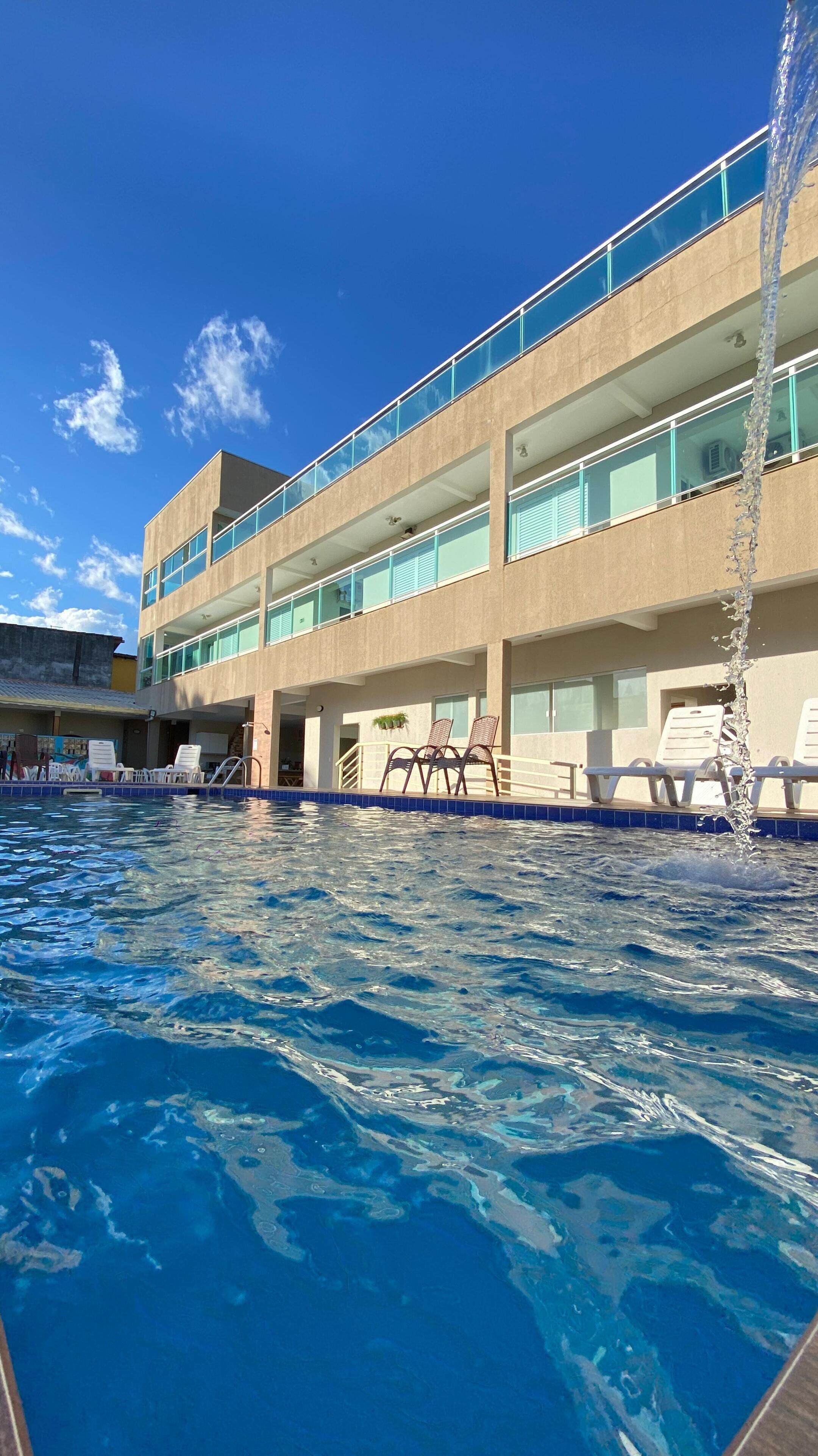 A hotel with a swimming pool, multiple balconies, and lounge chairs.