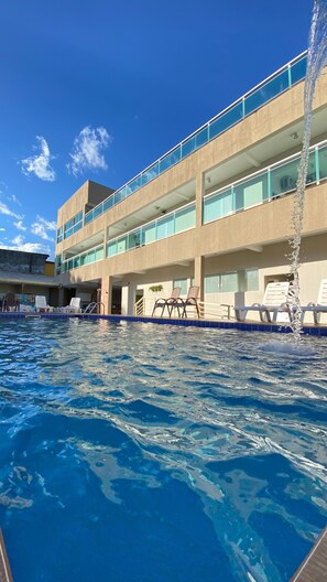 A hotel with a swimming pool, multiple balconies, and lounge chairs.