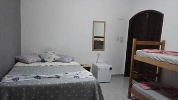 Un dormitorio con una cama, ventilador de techo, mesita de noche, espejo y literas.