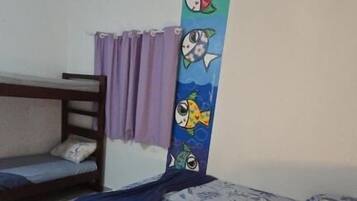 Um quarto com cama, beliche, parede com mural de peixes coloridos, cortina e mesa de cabeceira com luminária.