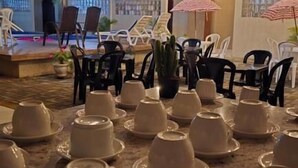 Un área de comedor al aire libre con mesas dispuestas, platos y tazones blancos, sillas y sombrillas.