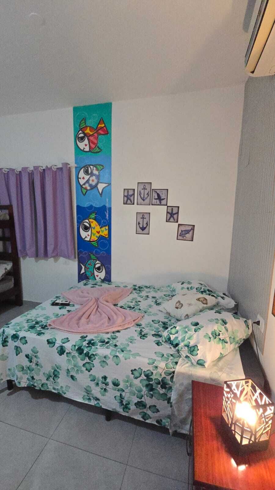 Un dormitorio con cama, una pared con cuadros, una ventana con cortinas y una mesita de noche con lámpara.