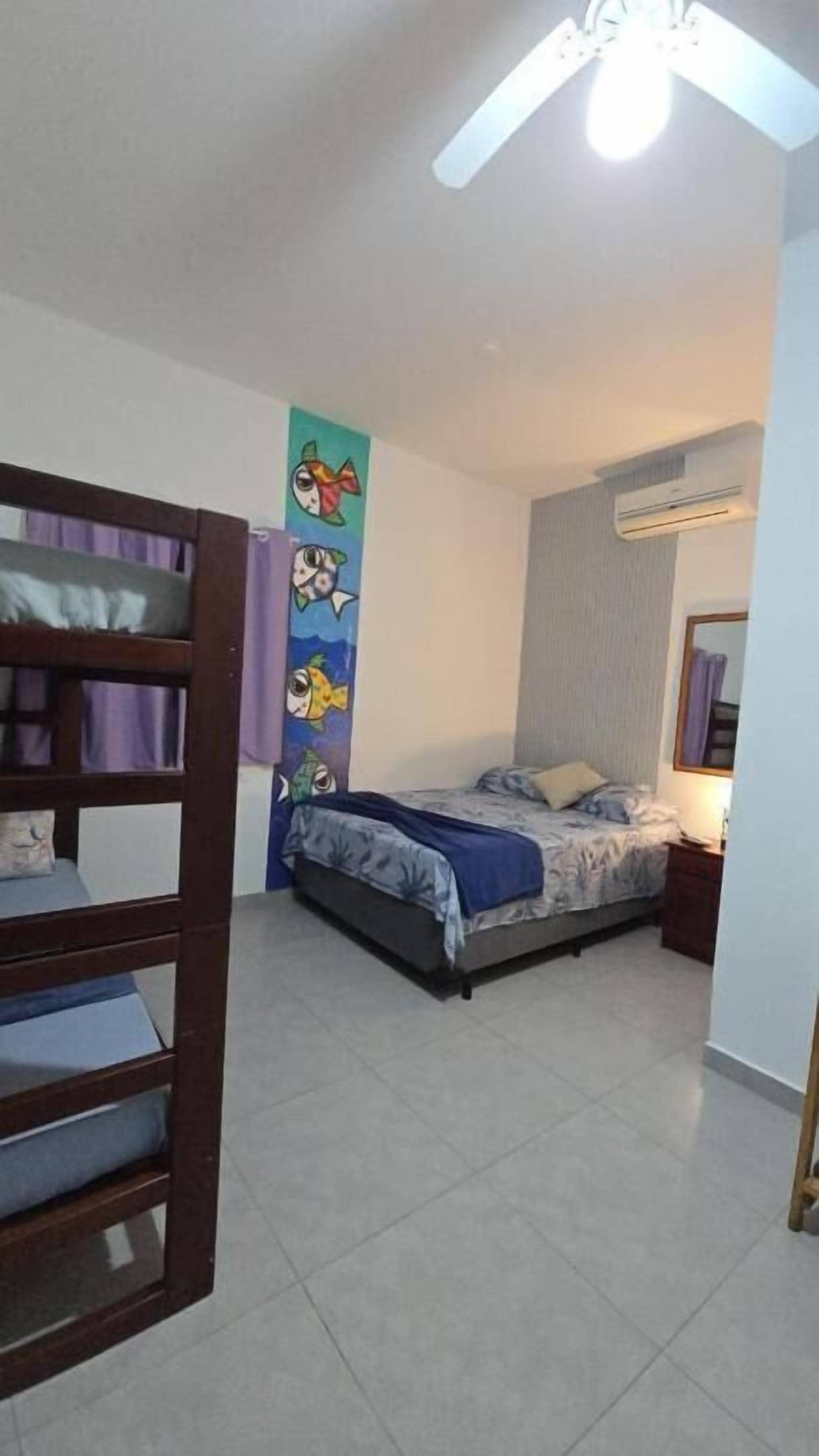 Een slaapkamer met stapelbedden, een bed met een blauwe deken, een plafondventilator en een airconditioning.