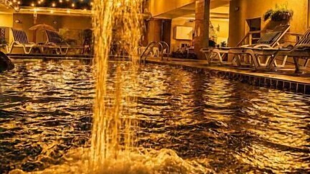 Escena nocturna con una fuente en un área de piscina, un edificio con balcones y vistas al cielo estrellado.