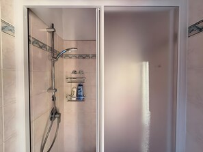 Eine bodenebene Dusche mit Handbrause, Wandarmatur und Ablagefläche für Pflegeprodukte.