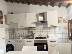 A compact kitchen with white cabinets, a gas stove, a built-in oven, and a washing machine.