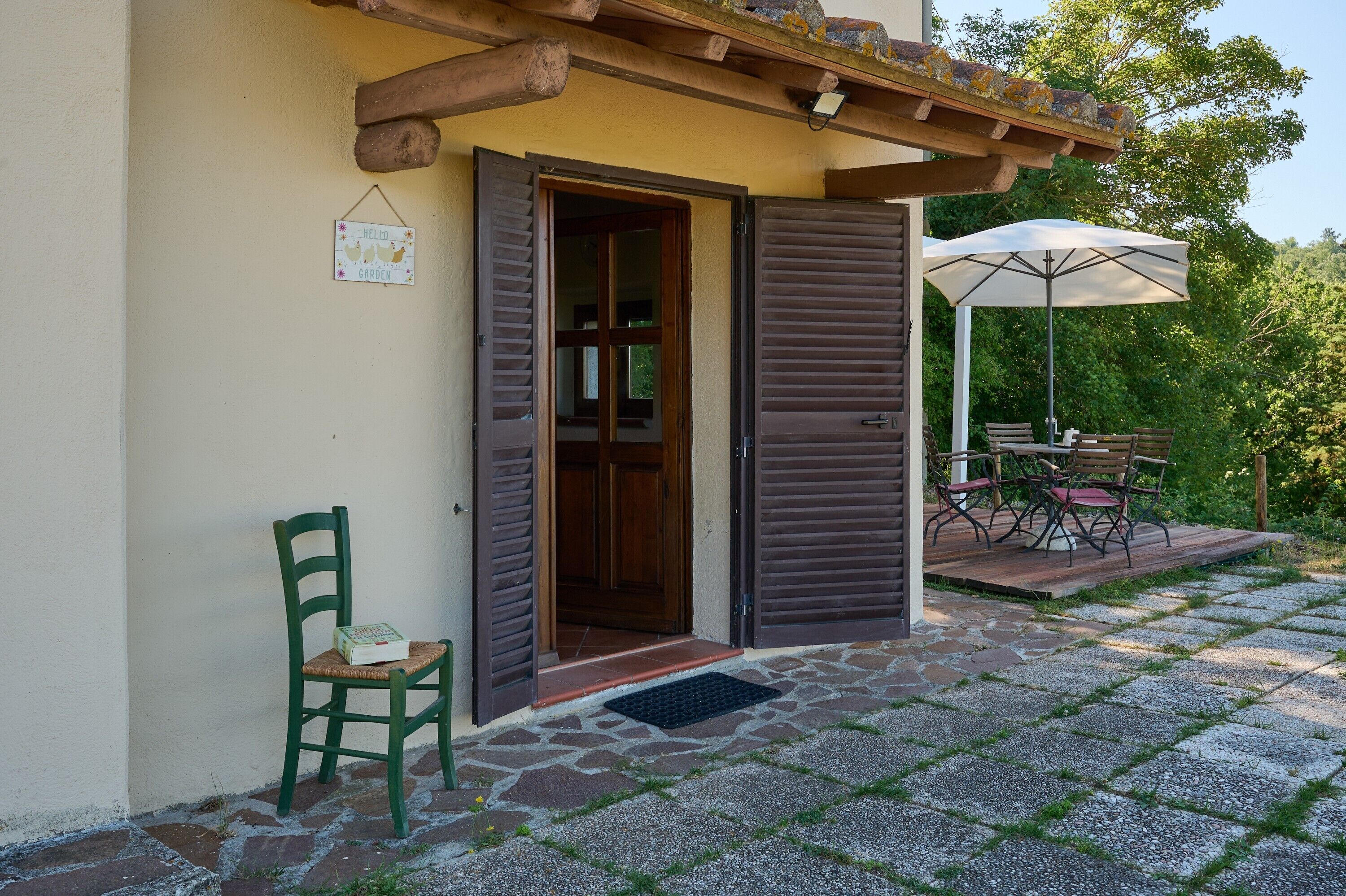 Ein Haus mit Holztür, einem grünen Stuhl und einer Terrasse mit Tisch und Sonnenschirm.
