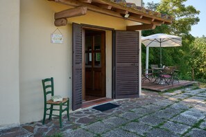 A house with a wooden door, a green chair, and a patio with a table and umbrella.