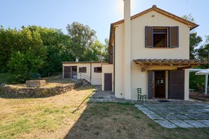 Ein zweistöckiges Haus mit einem Steinweg, der zum Eingang führt, einer kleinen Terrasse und einem Garten mit Bäumen.