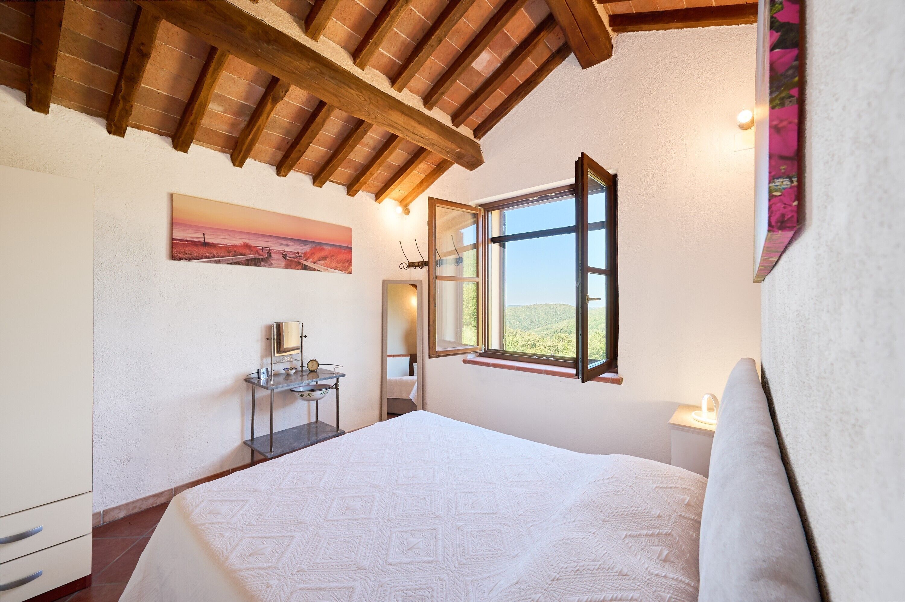 Una camera da letto con un letto, un comodino, uno specchio, una finestra e un quadro appeso al muro.
