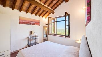 Una camera da letto con un letto, un comodino, uno specchio, una finestra e un quadro appeso al muro.