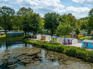 Een rij kleurrijke stacaravans aan een rustige rivier, omringd door weelderige begroeiing.