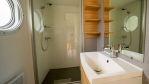 A modern bathroom with a glass-enclosed shower, a white sink, and wooden shelves. - Holiday Home in Amstelveen With Terrace (Amstelveen)