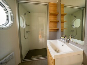 Een moderne badkamer met een douchecabine van glas, een witte wastafel en houten planken.