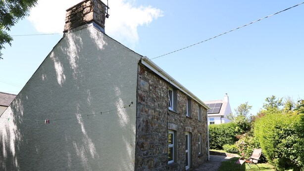Une maison en pierre à l’extérieur blanc, avec une cheminée et un petit jardin agrémenté d’une chaise.