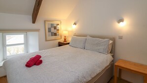 Une chambre à coucher avec un lit, une table de chevet, une lampe, un tableau encadré et une fenêtre.
