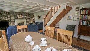 Un coin repas avec une table préparée pour le thé, une cheminée, un escalier et une bibliothèque.