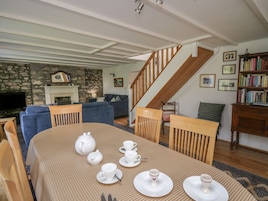 Un comedor con una mesa lista para el té, una chimenea, una escalera y una estantería.