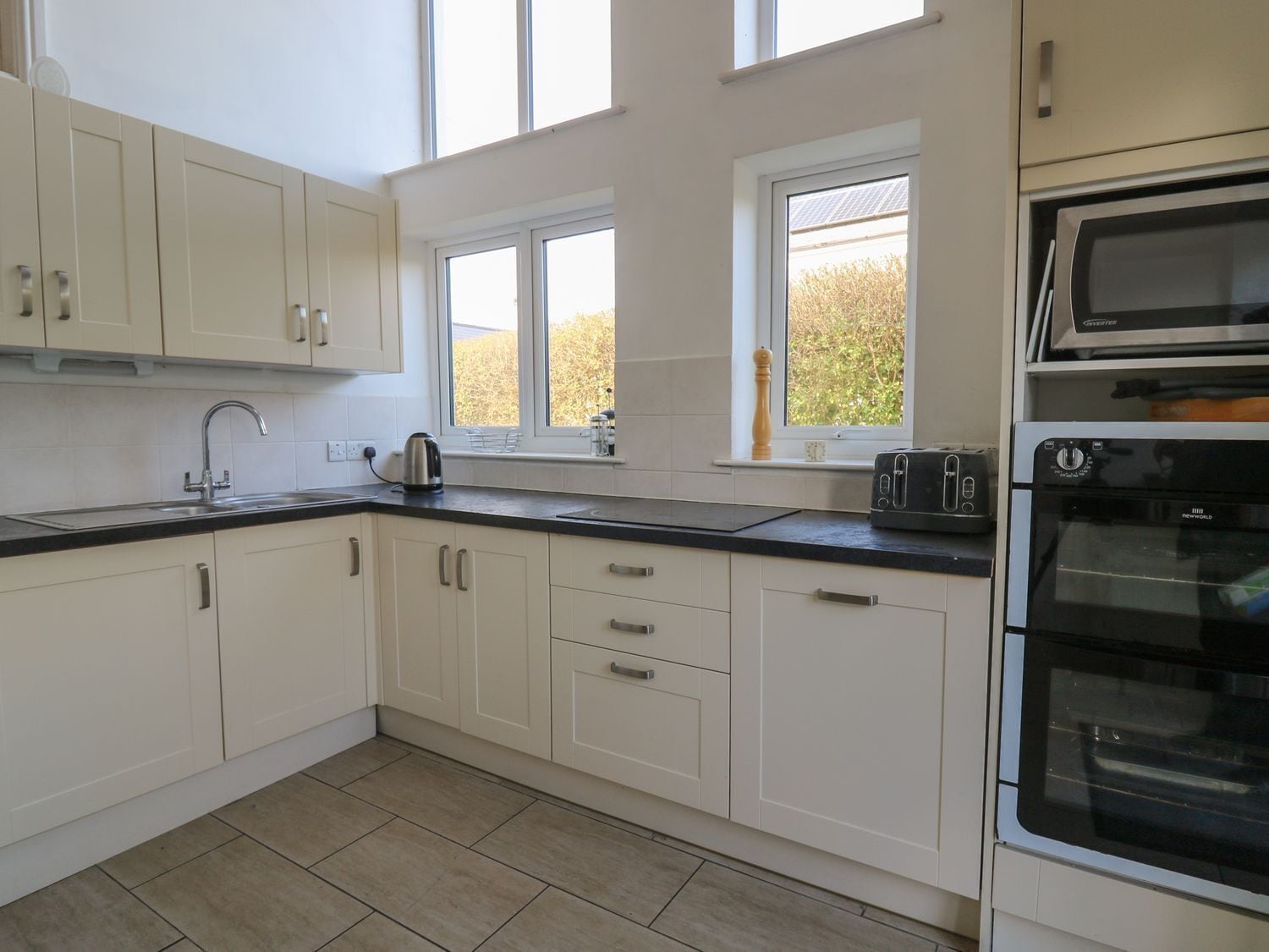 A modern kitchen with white cabinets, a black countertop, a built-in oven, and a window with a view of trees.