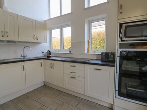 A modern kitchen with white cabinets, a black countertop, a built-in oven, and a window with a view of trees. - Tegfan (Newport)