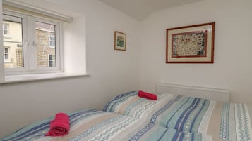 A bedroom with a window, two beds with patterned bedding, a radiator, and two framed pictures on the wall.