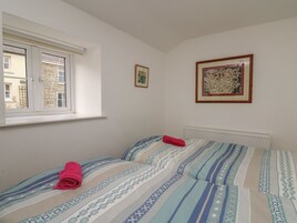 Un dormitorio con ventana, dos camas con ropa de cama estampada, un radiador y dos cuadros en la pared.