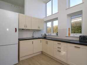 Una cocina con armarios blancos, encimera negra, horno empotrado, fregadero y ventana con vistas a zonas verdes.