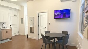 A modern kitchen with white cabinets, a dining area with a round table and chairs, and a flat-screen TV mounted on the wall.