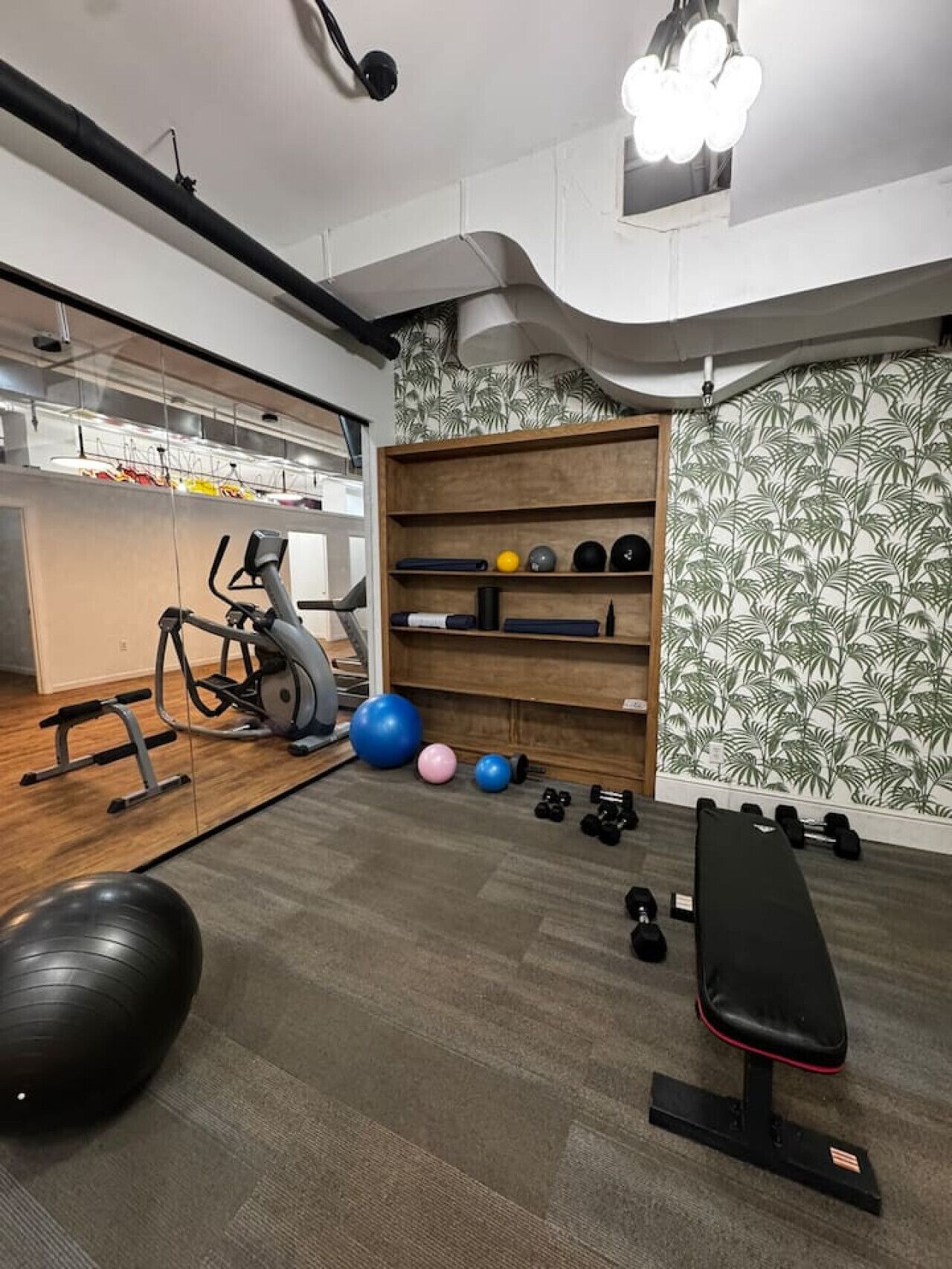 Ginásio em casa com equipamento de exercícios, um banco e uma parede com padrão de folhas.