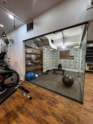 Ein Fitnessraum mit Trainingsgeräten, einem Spiegel und einer Wand mit Muster.