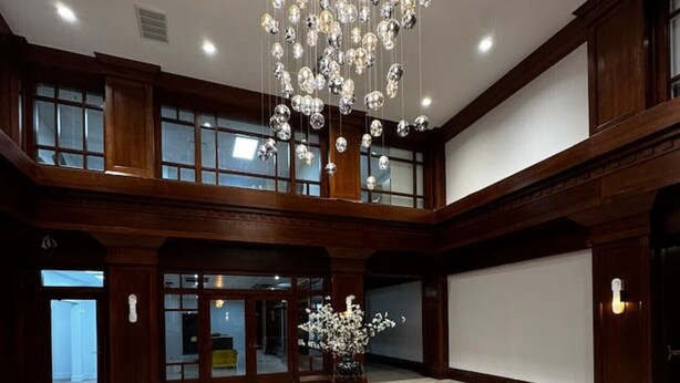 A spacious lobby with a large chandelier, a central round table with a vase, and a checkered floor.